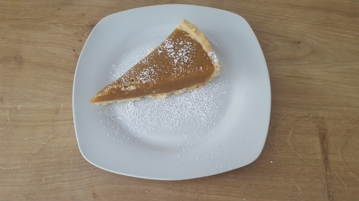 slice of caramel coloured tart on white plate dusted with icing sugar