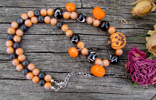 orange and black necklace with a pumpkin charm displayed on a rustic wooden block background for halloween pumpkin art