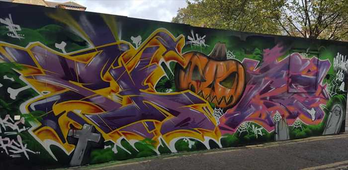 green wall painted with street art of an orange pumpkin with purple graffiti lettering either side