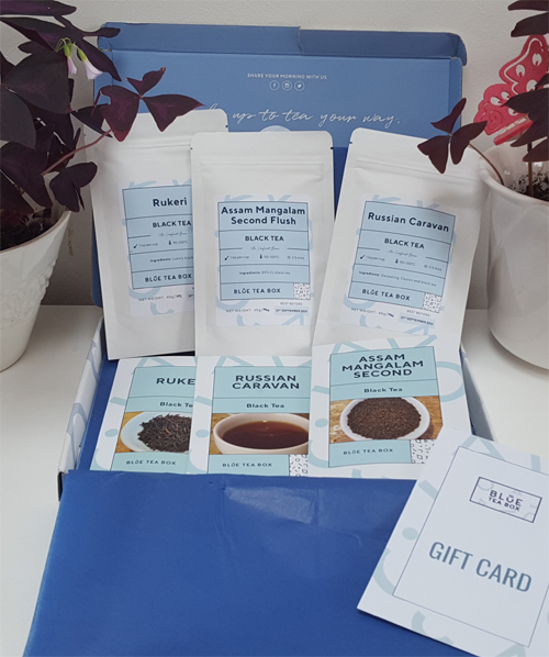 an open blue box lined with blue tissue and three packs of tea with info cards picturing the types of tea, some strands and a cup of black tea
